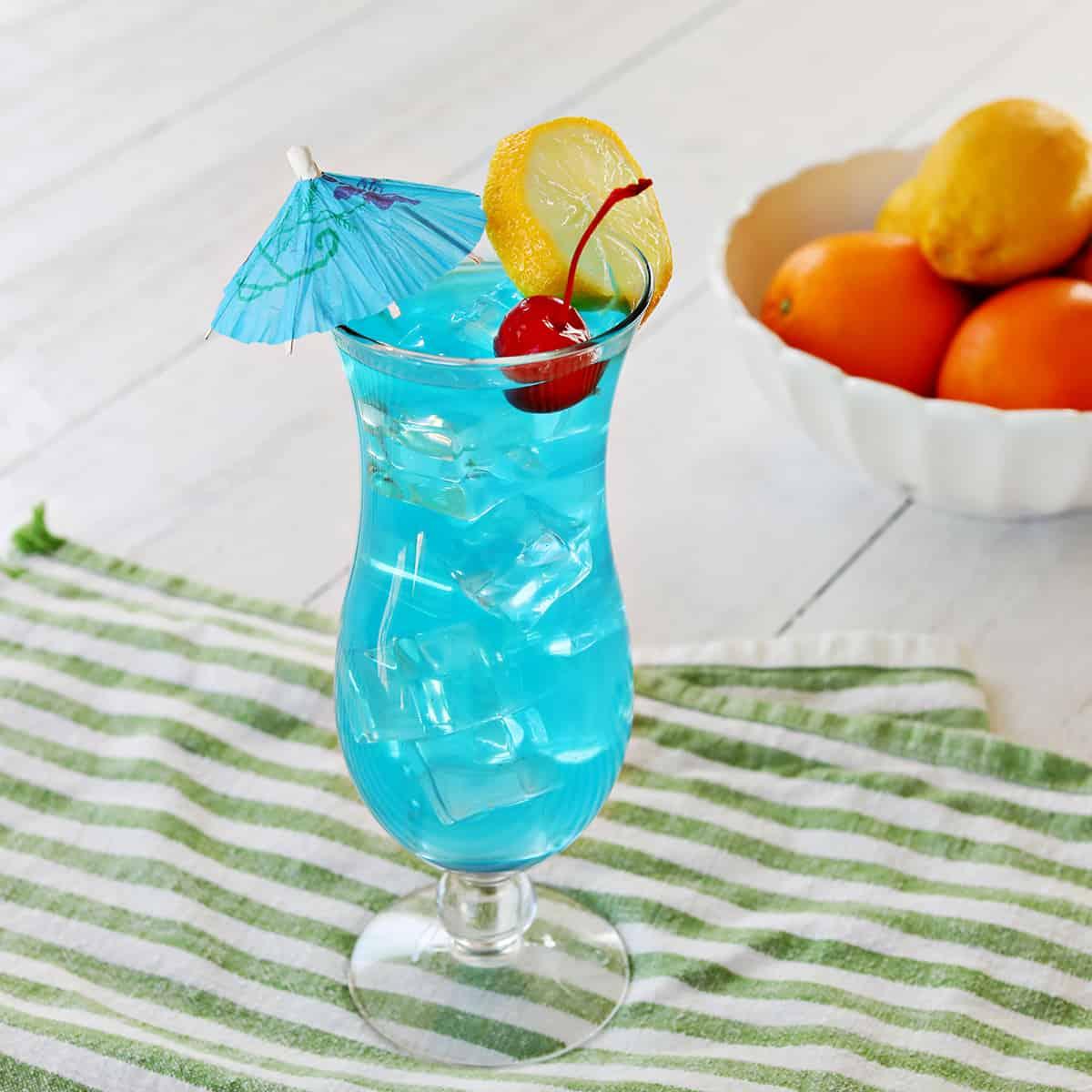 Vibrant blue Electric Blue Lagoon cocktail in a highball glass with ice and orange slice garnish