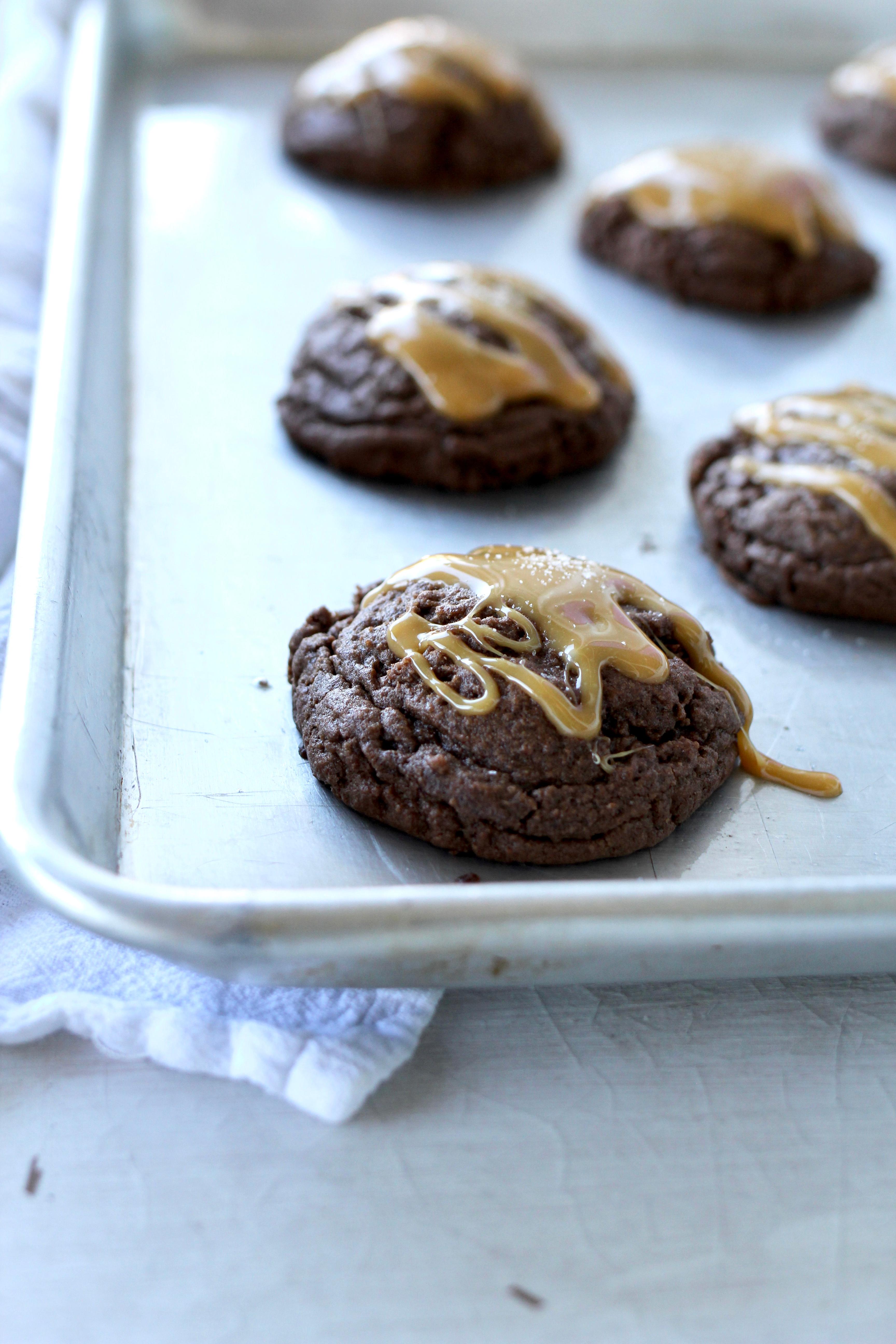 Close-up shot of salted caramel brownie cookies on a baking sheet, with a drizzled caramel sauce