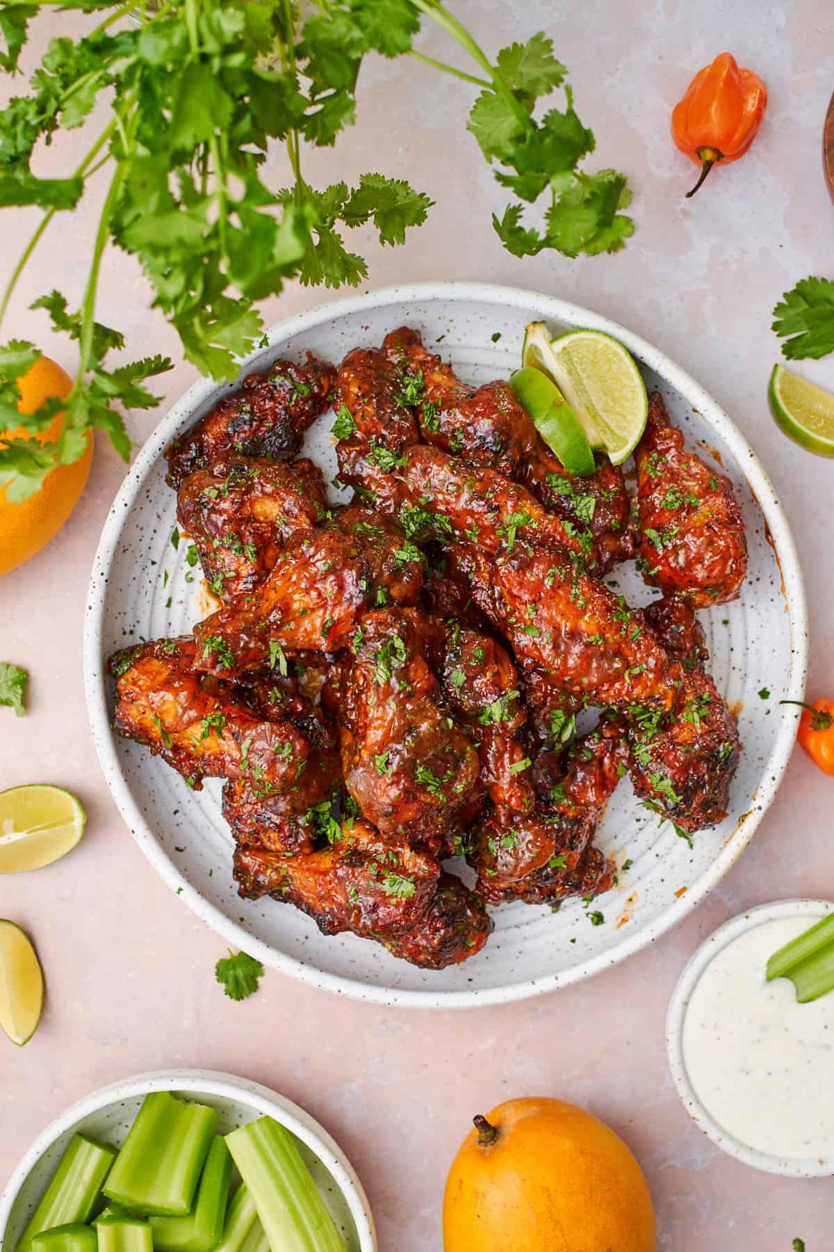 A platter of mango habanero chicken wings, garnished with cilantro and lime wedges