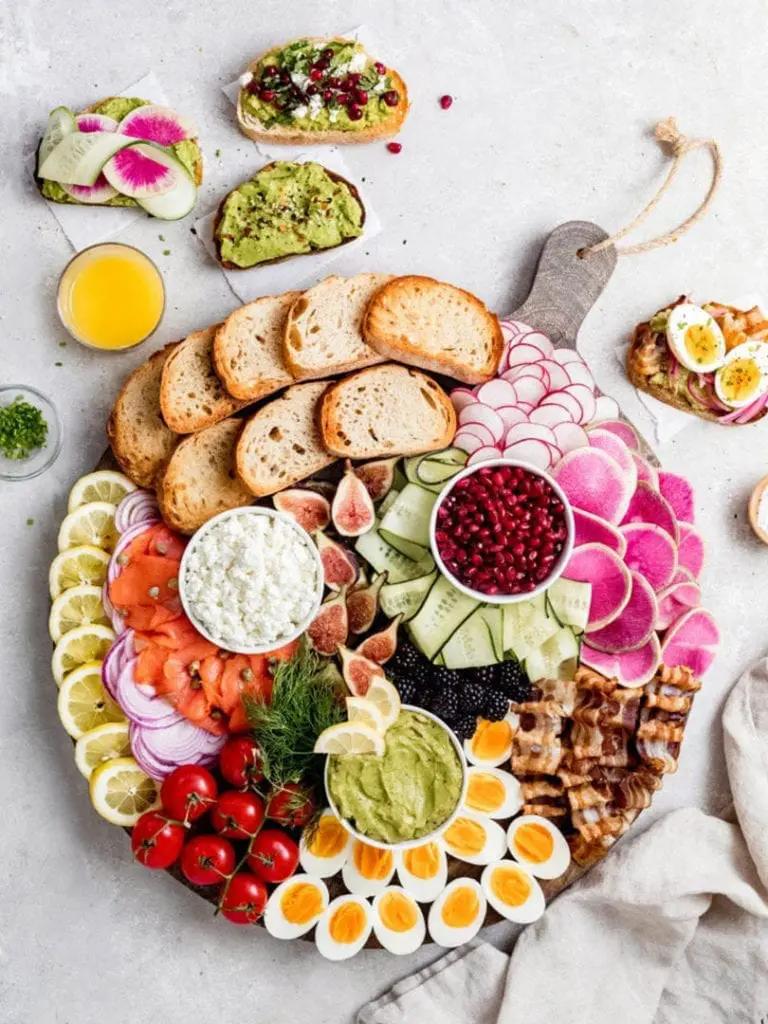 overhead shot of several slices of roasted red pepper and goat cheese avocado toast arranged on a wooden board