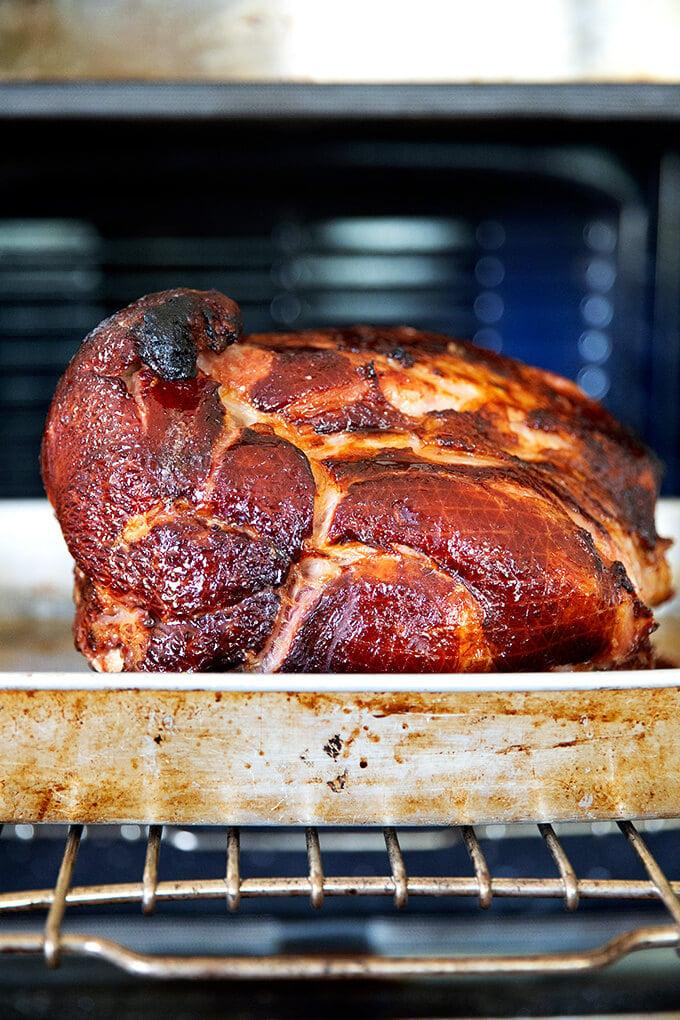 christmas ham being basted with glaze in a roasting pan