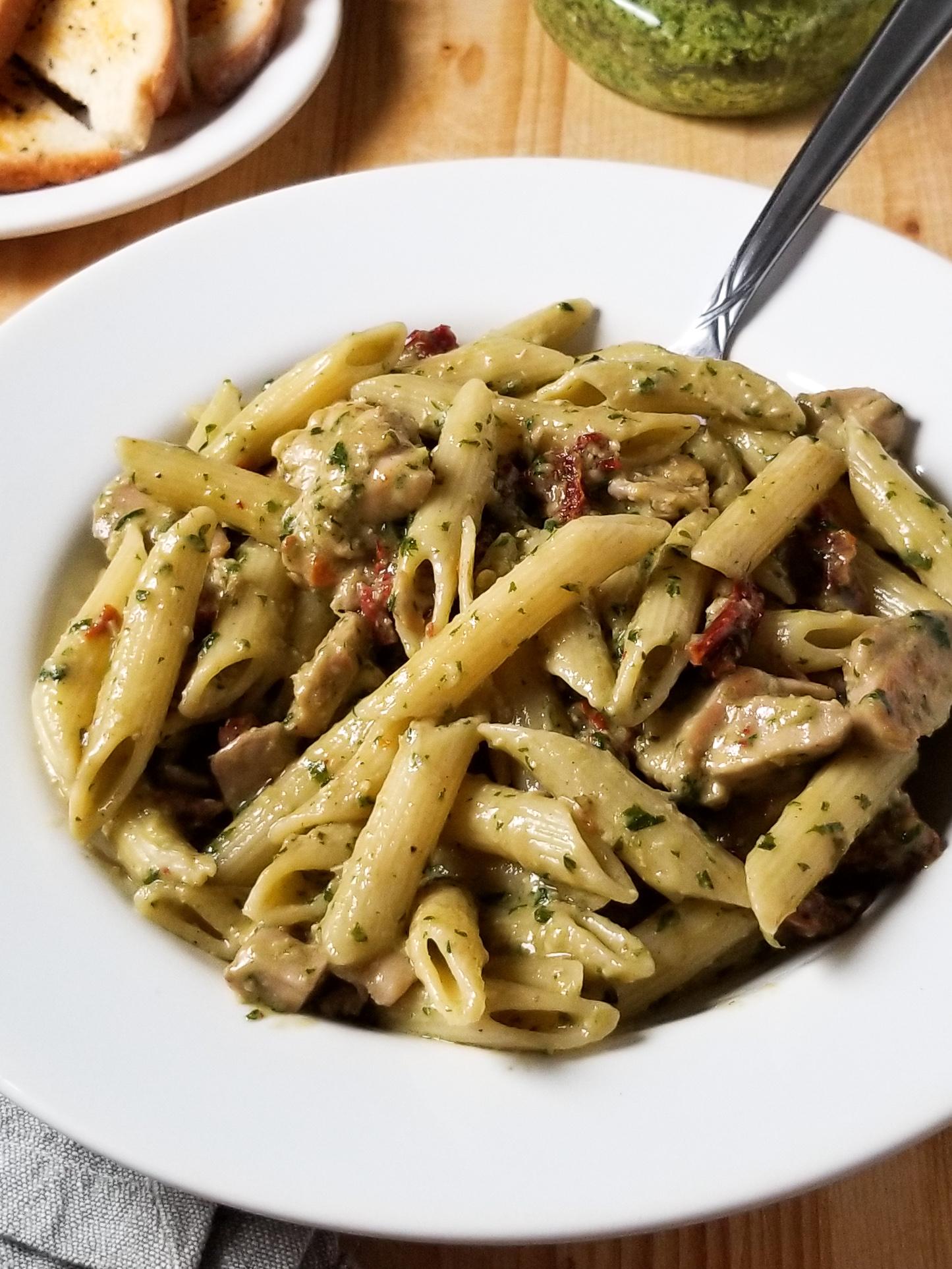 Creamy pesto pasta with chicken and sun-dried tomatoes in a rustic setting