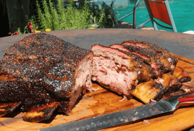 Close-up shot of perfectly smoked Texas-style ribs, glistening with barbecue sauce, on a wooden cutting board.