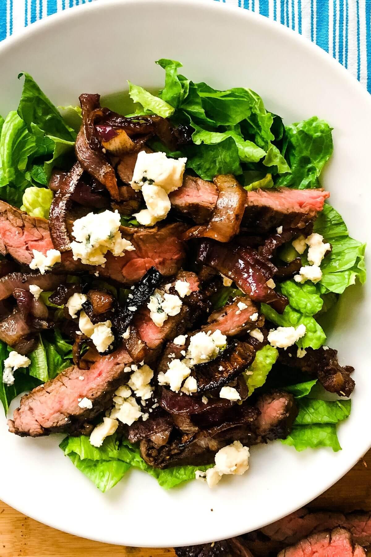 A vibrant steak salad with blue cheese, caramelized onions, and mixed greens