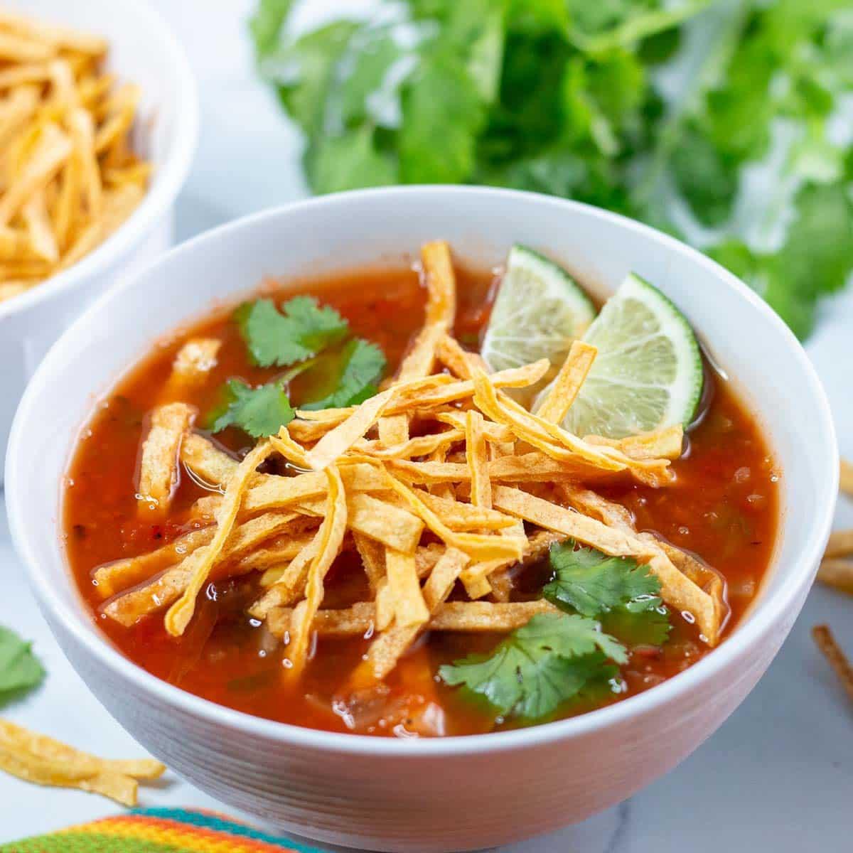 A bowl of vibrant red Spicy Vegan Tortilla Soup garnished with fresh cilantro and avocado