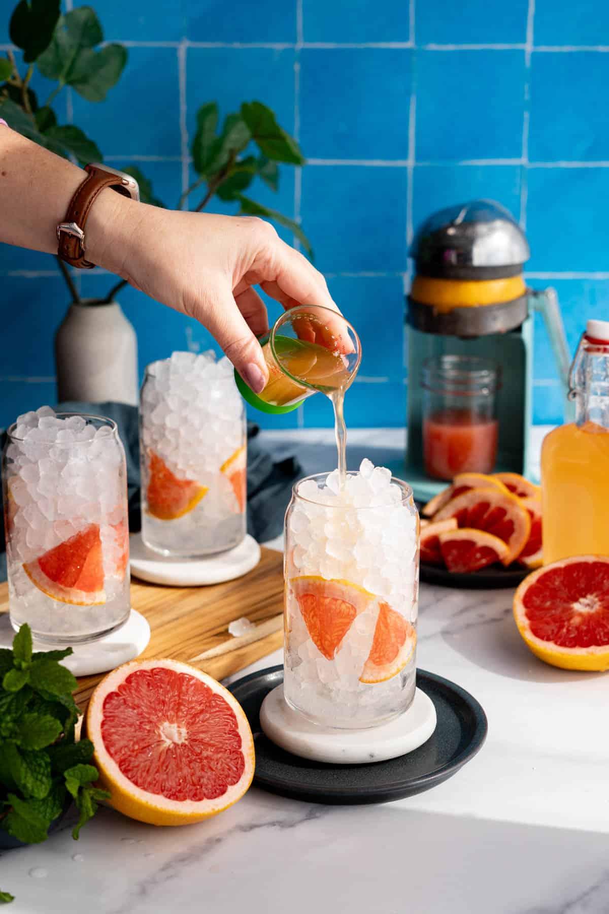 hand pouring grapefruit lemonade into a glass with ice and a slice of grapefruit