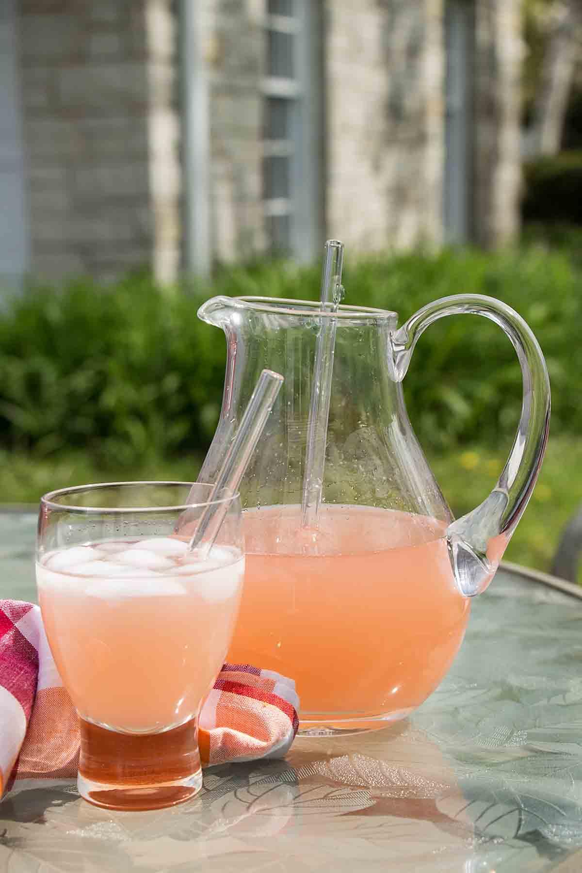 A pitcher of Strawberry Rhubarb Lemonade on a picnic table, surrounded by summer flowers