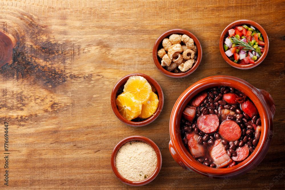 A rustic wooden table set with a steaming bowl of Feijoada and a glass of Brazilian wine, with rain falling outside a window
