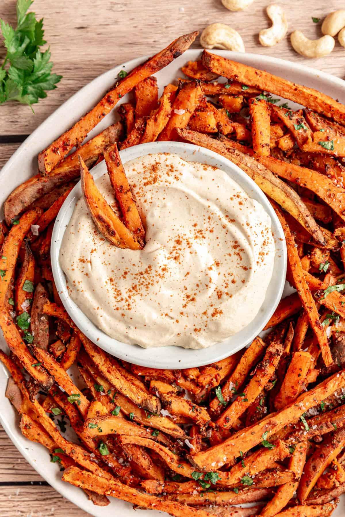 A table set for a casual outdoor dinner, featuring a platter of grilled sweet potato fries and a bowl of garlic aioli.