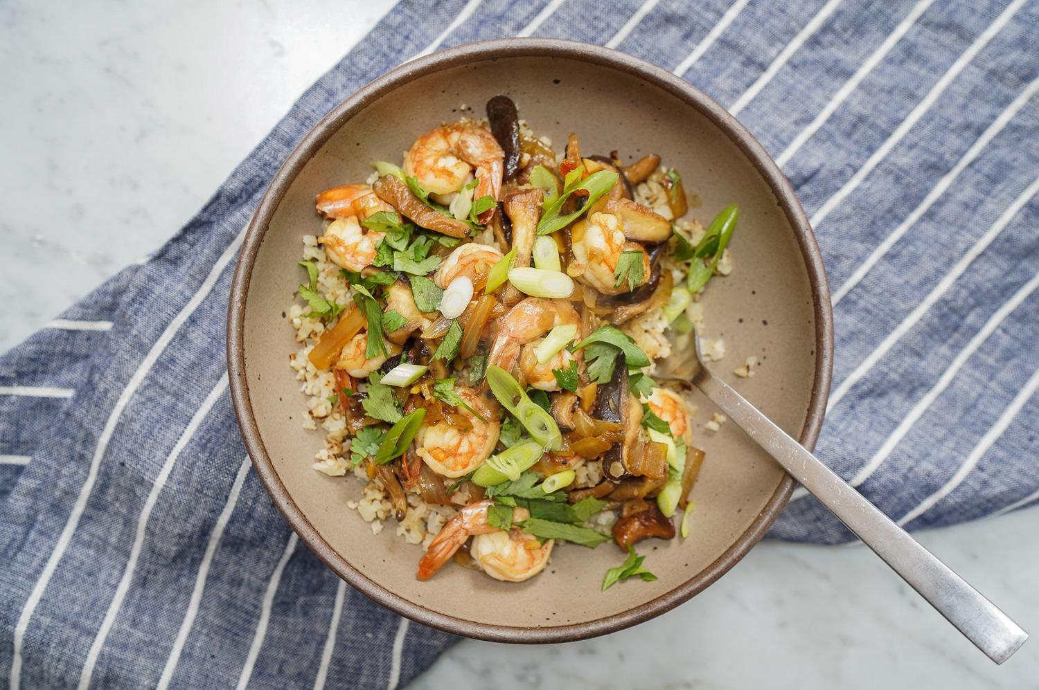 A person enjoying a plate of cauliflower rice with shrimp stir-fry