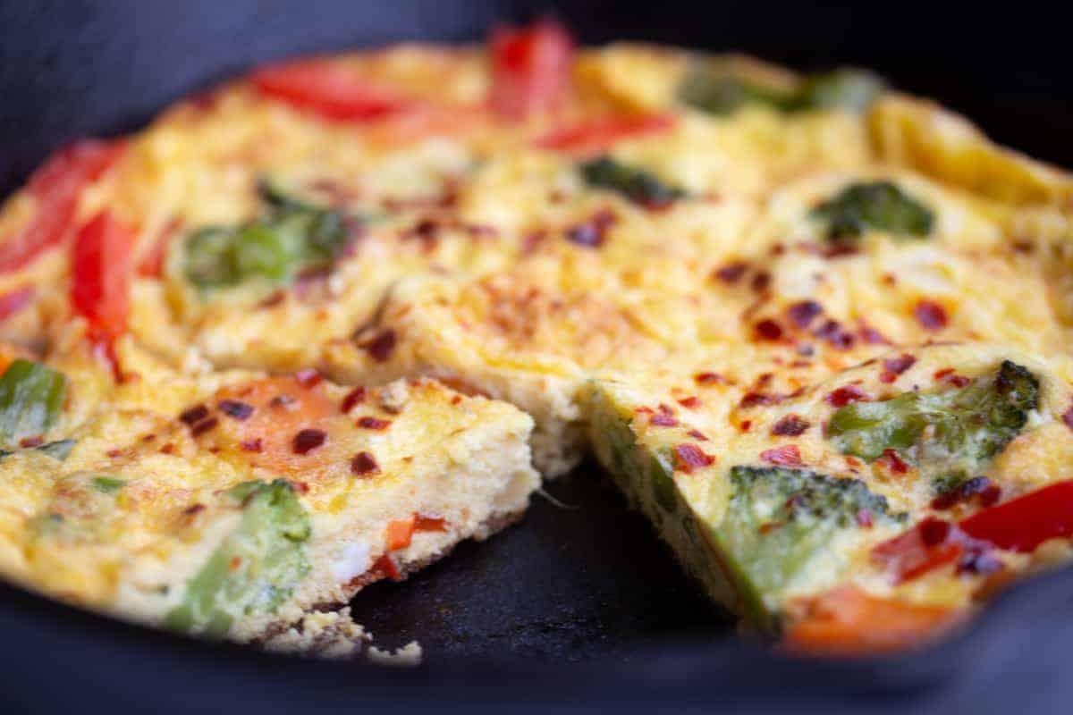 Close up shot of a slice of Creamy Gruyere & Leftover Vegetable Frittata showing the creamy texture and vegetables.