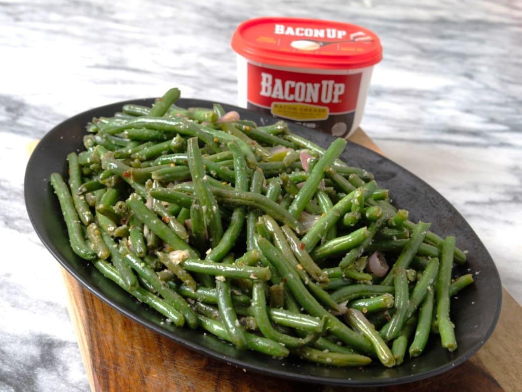 close-up of green beans and bacon in a skillet with cooking utensils