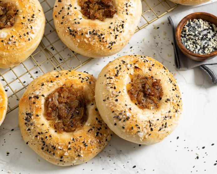 Close-up shot of golden-brown Everything Bagel Muffins, slightly crumbly, with sesame seeds, poppy seeds, and dried onion flakes visible on top