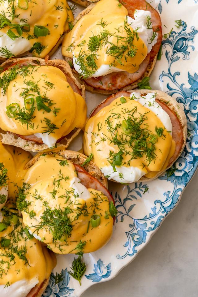 Person carefully pouring Basil Hollandaise sauce over a poached egg on an English muffin