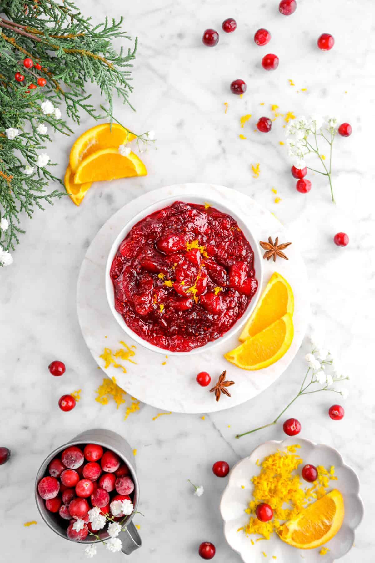 A bowl of cranberry sauce dip with orange zest, garnished with fresh cranberries and orange slices, sitting on a rustic wooden table