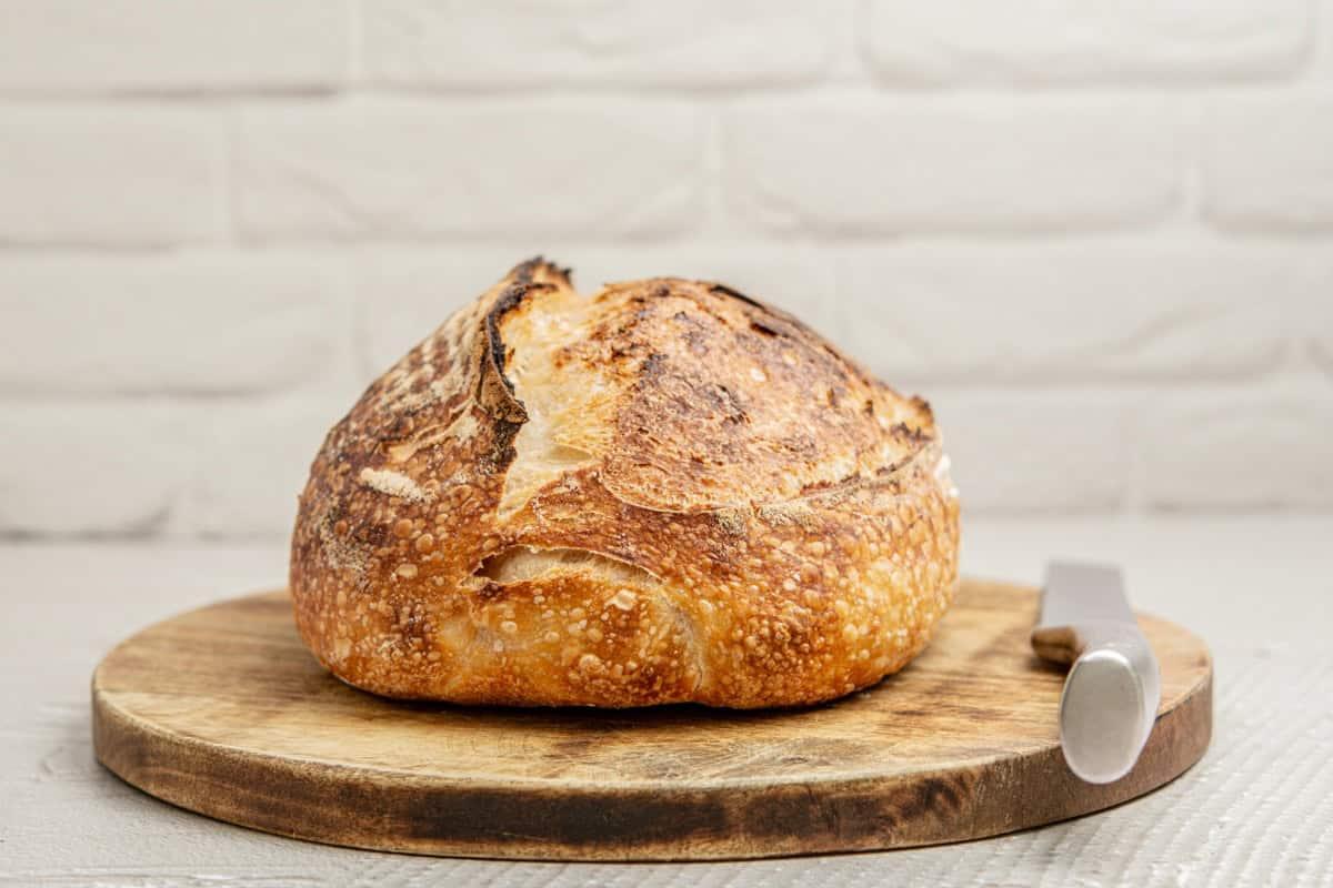 A rustic sourdough loaf, golden brown and crusty, on a wooden cutting board