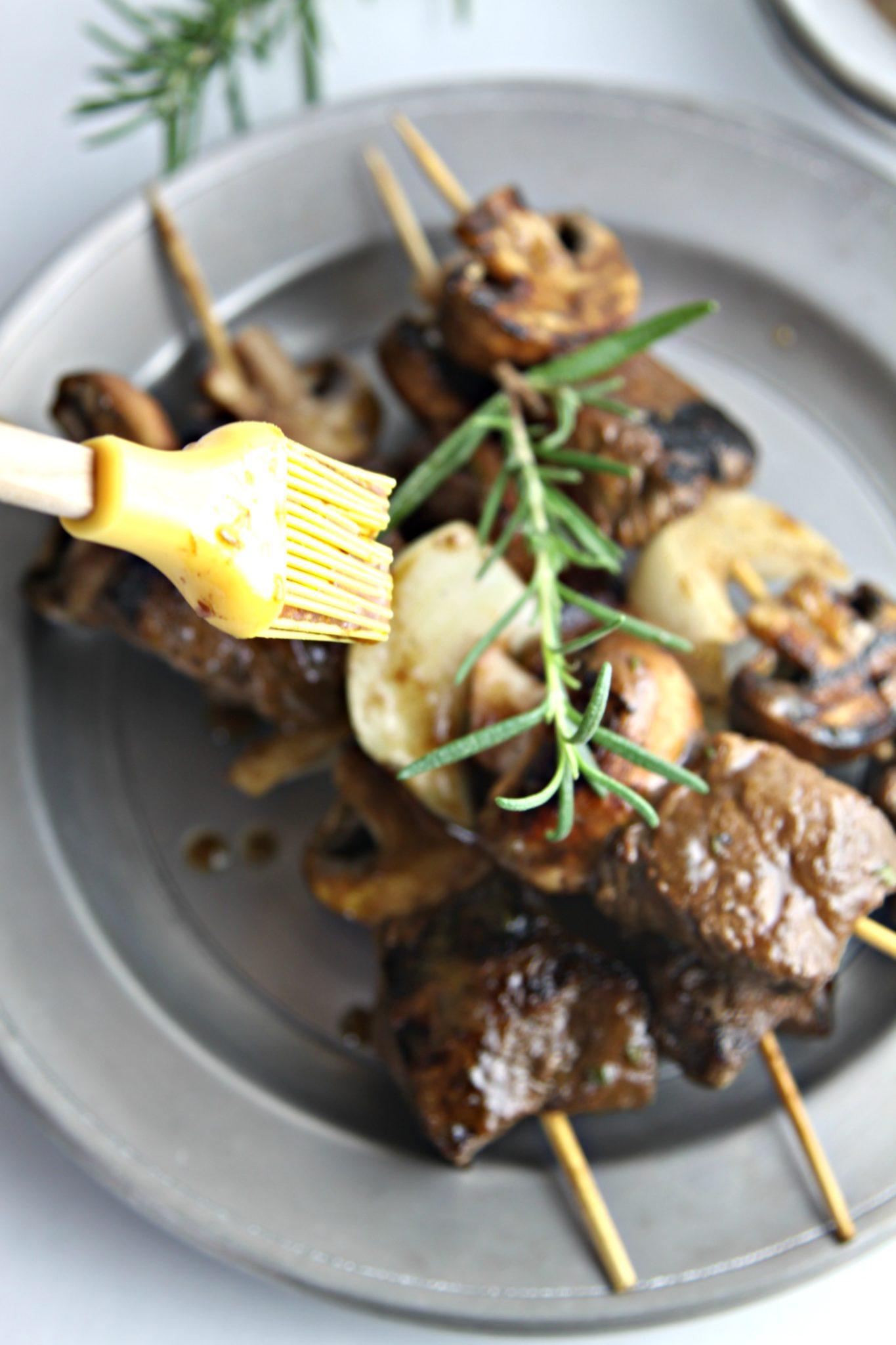 A person carefully threading beef and mushrooms onto skewers