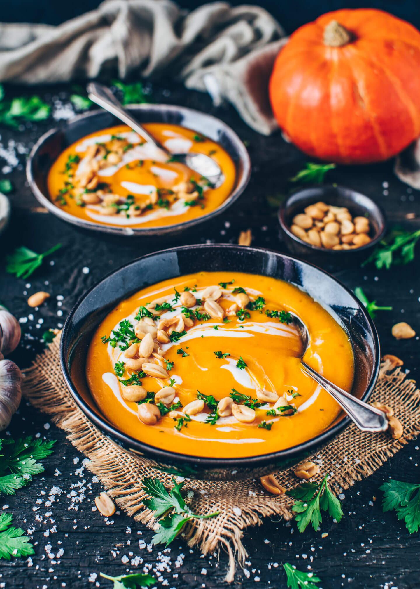 Close-up shot of a bowl of creamy pumpkin soup garnished with toasted pepitas and a swirl of cream.