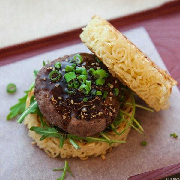 Close-up shot of a delicious ramen burger with mirin glaze, garnished with sesame seeds