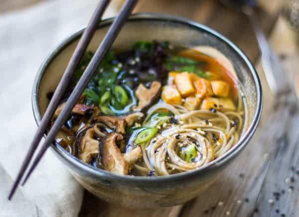 person adding sriracha to a bowl of tofu noodle soup
