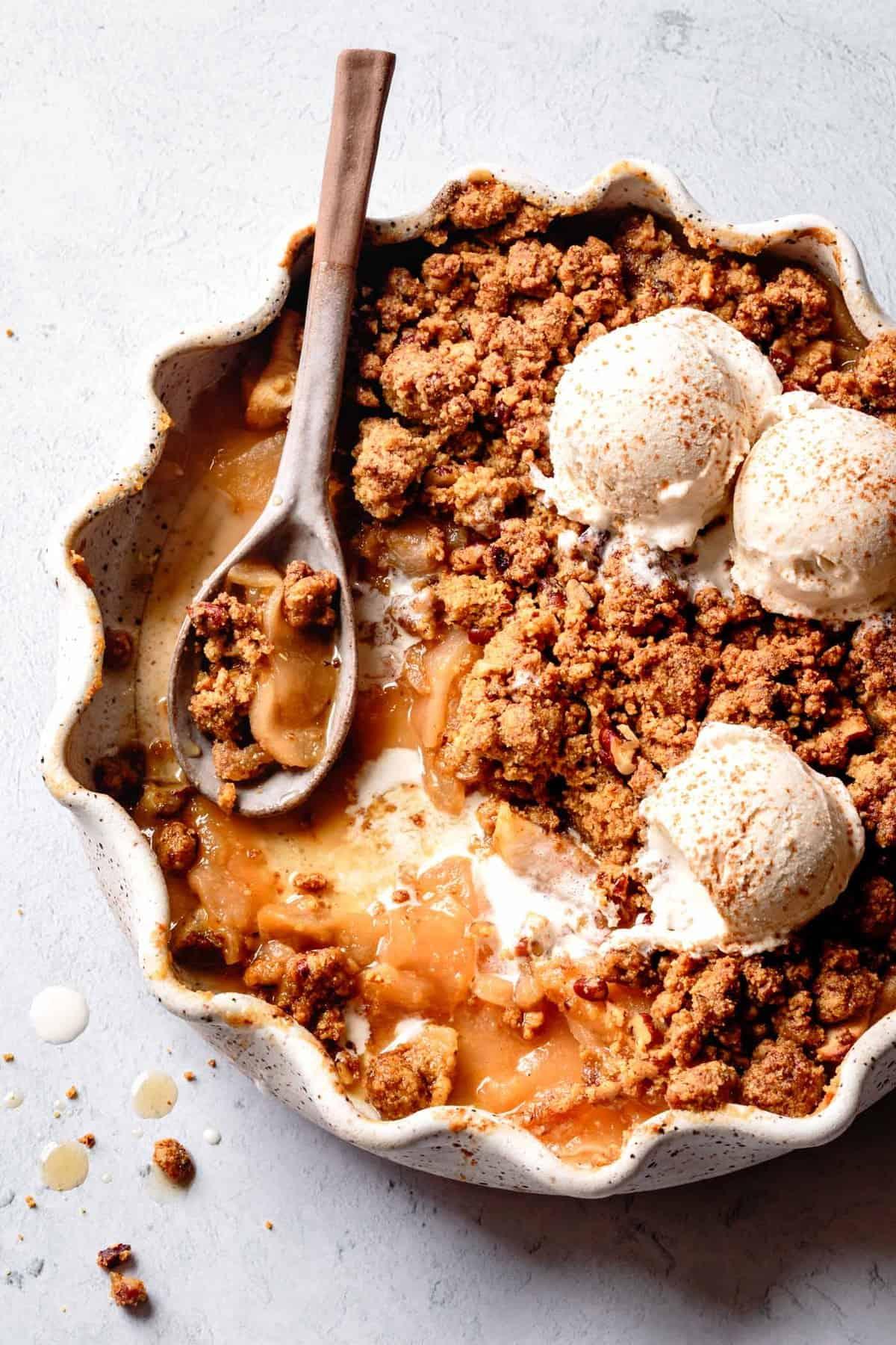 A rustic, golden-brown apple crisp with a coconut-almond topping, served warm with a scoop of vanilla ice cream