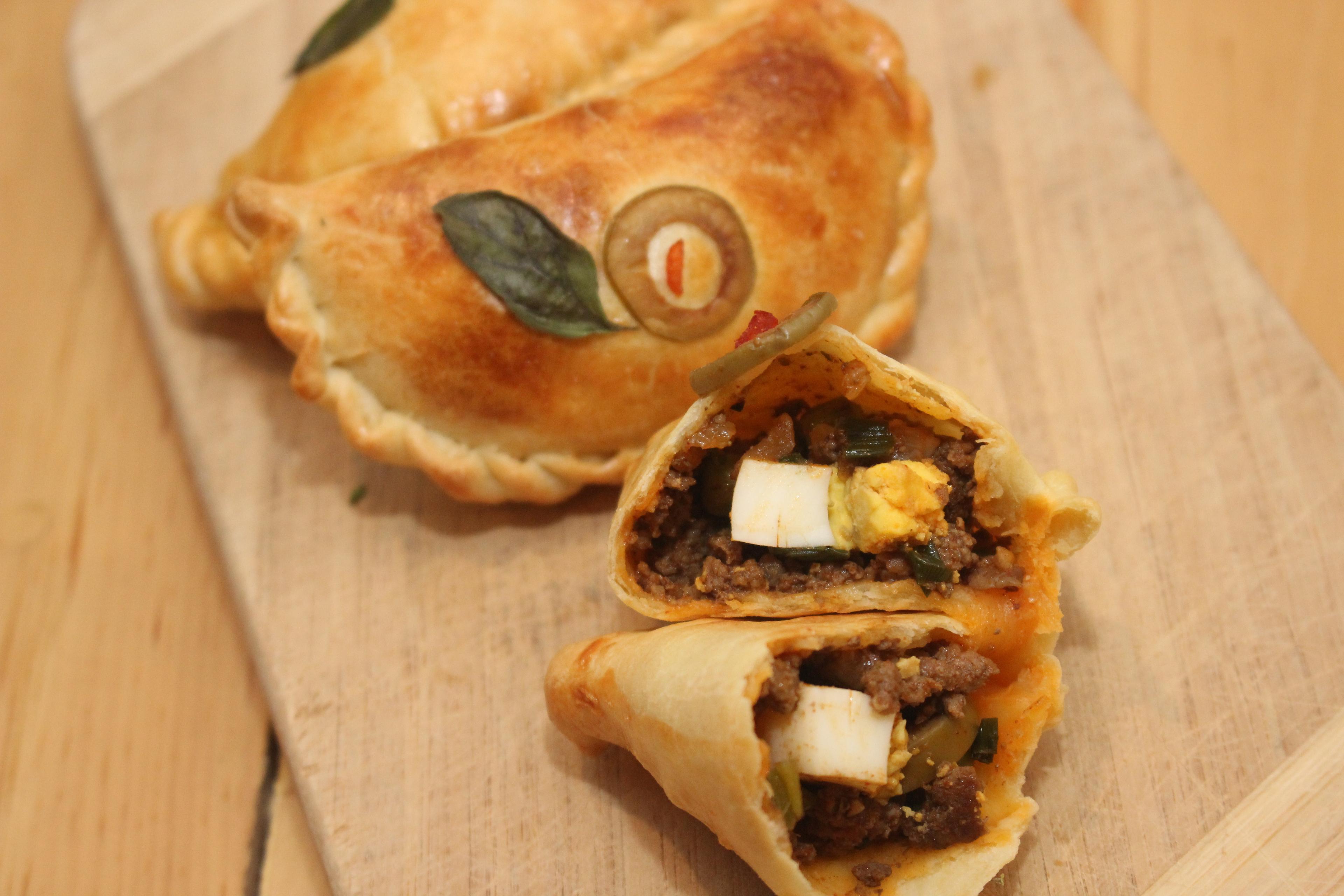 Close-up of a single carne asada empanada, cut open to show the filling and chimichurri
