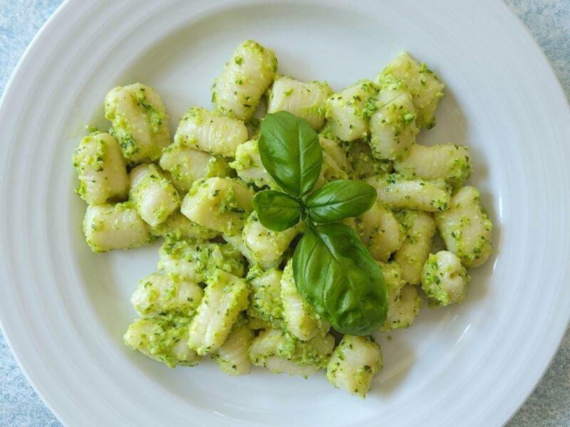 Close-up shot of a plate of pasta with gnocchi and pesto, with steam rising