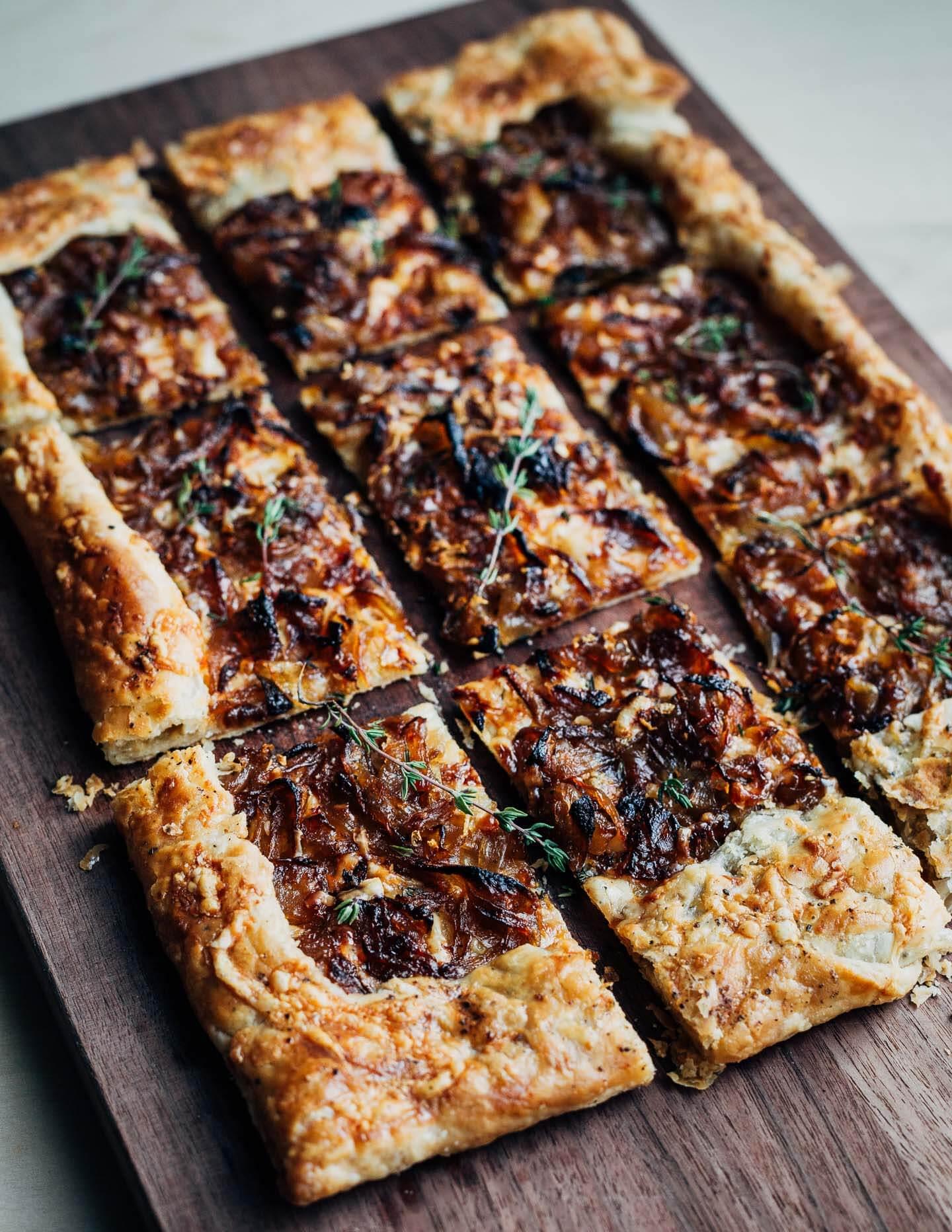 A rustic, golden-brown paprika and caramelized onion tart on a wooden cutting board, garnished with fresh parsley