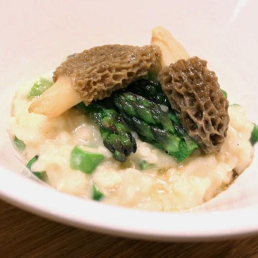 a person stirring asparagus risotto with morels in a pot on the stove