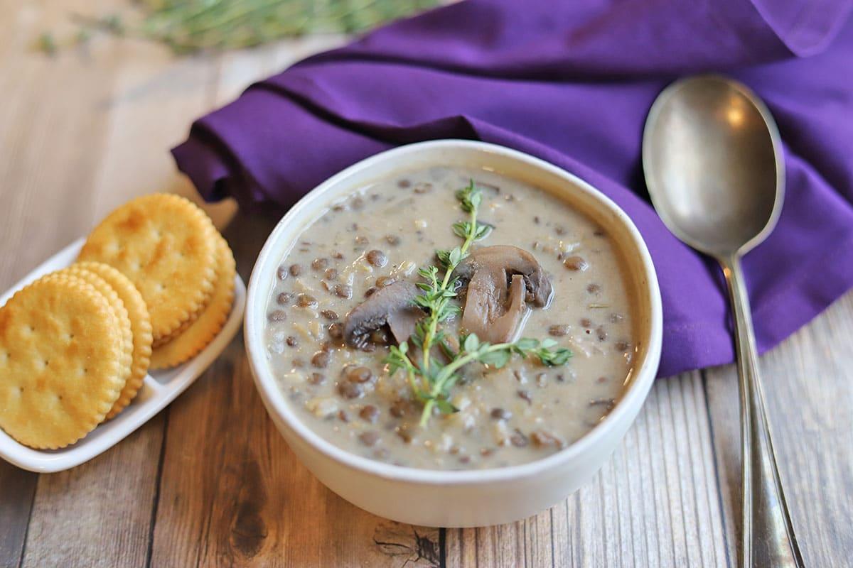 pouring creamy lentil mushroom stroganoff soup into a rustic bowl
