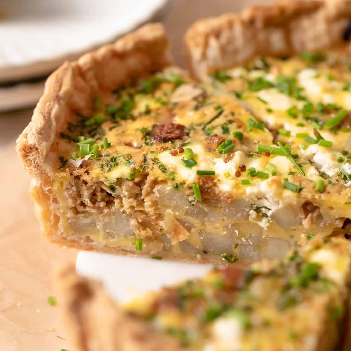 A golden brown quiche with puff pastry crust, showing a creamy filling and some herbs