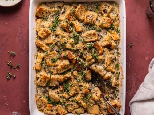 Overhead shot of uncooked savory bread pudding in a baking dish, showing bread cubes, cheese, and thyme, ready to go into the oven