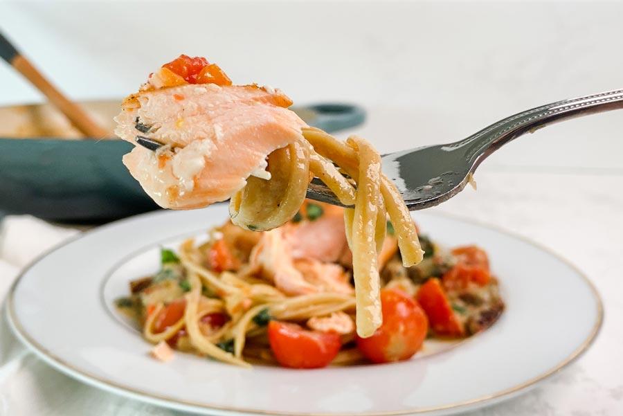 close-up shot of a fork lifting creamy tuscan salmon pasta from a bowl