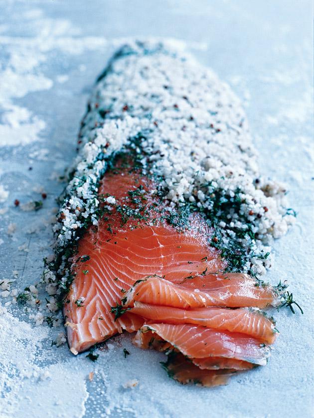 Close-up shot of salmon fillets being cured with a mixture of salt, sugar, and fresh dill