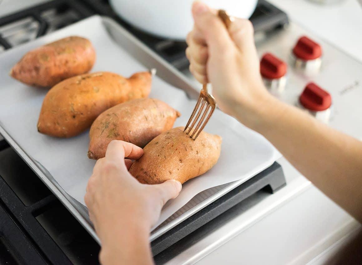 A close up shot of a hand reaching for a roasted sweet potato