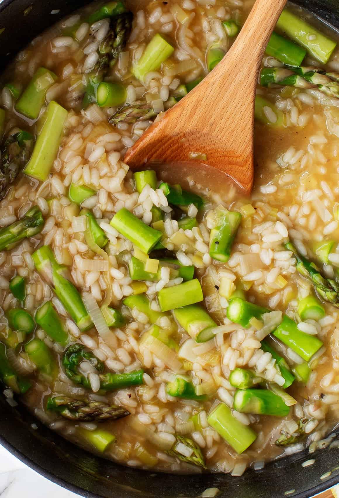 Close-up shot of a bowl of creamy asparagus and potato risotto, garnished with fresh parsley and Parmesan cheese.