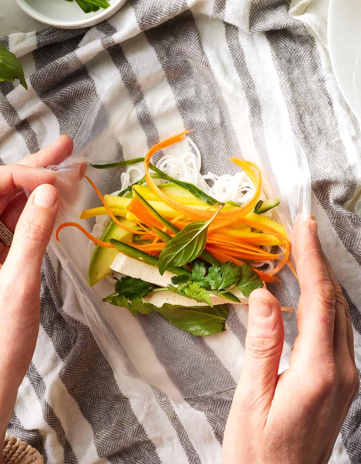 A person preparing a spring roll with various fresh vegetables