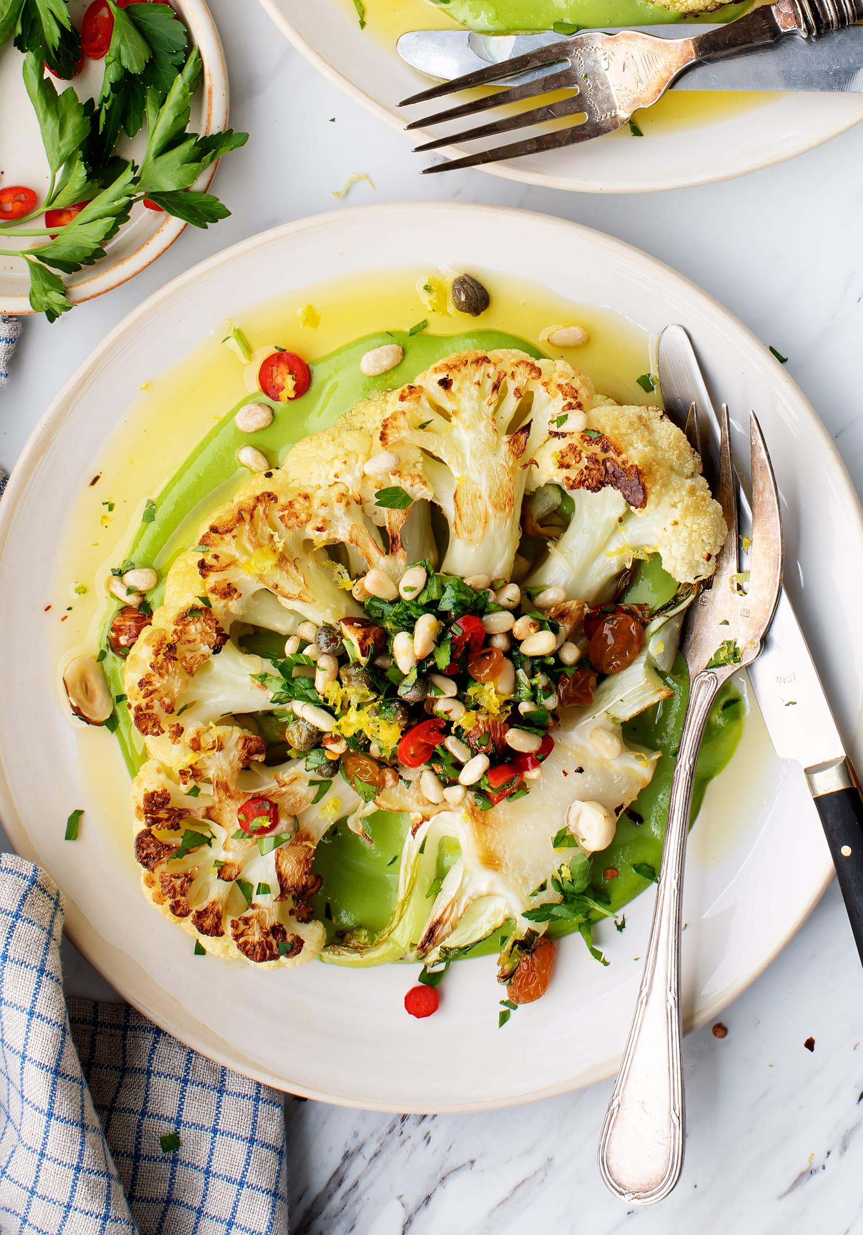 A beautifully roasted cauliflower steak alongside vibrant broccoli florets, garnished with fresh herbs.
