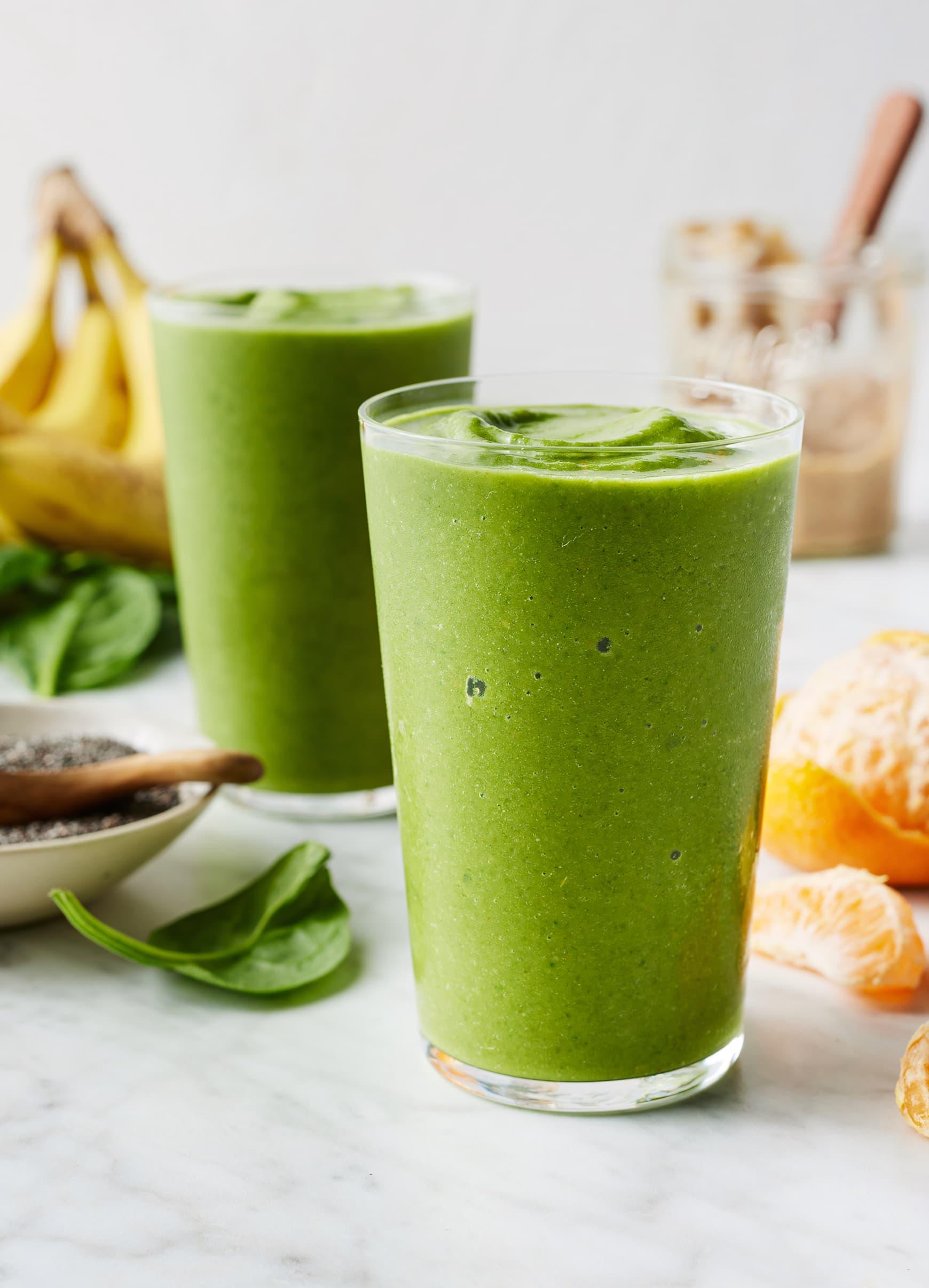 Various fresh ingredients for a green smoothie, such as bananas, spinach, chia seeds, and berries.