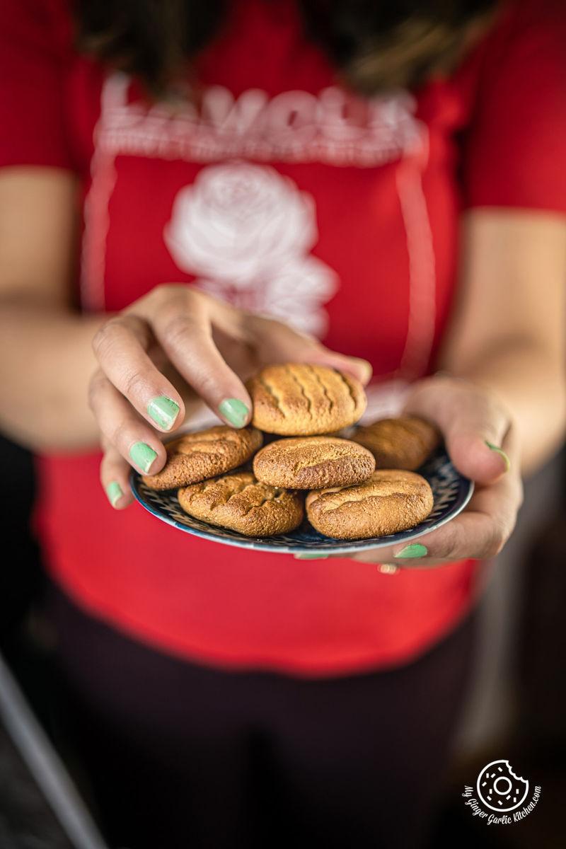 A person holding a plate with a few almond cookies