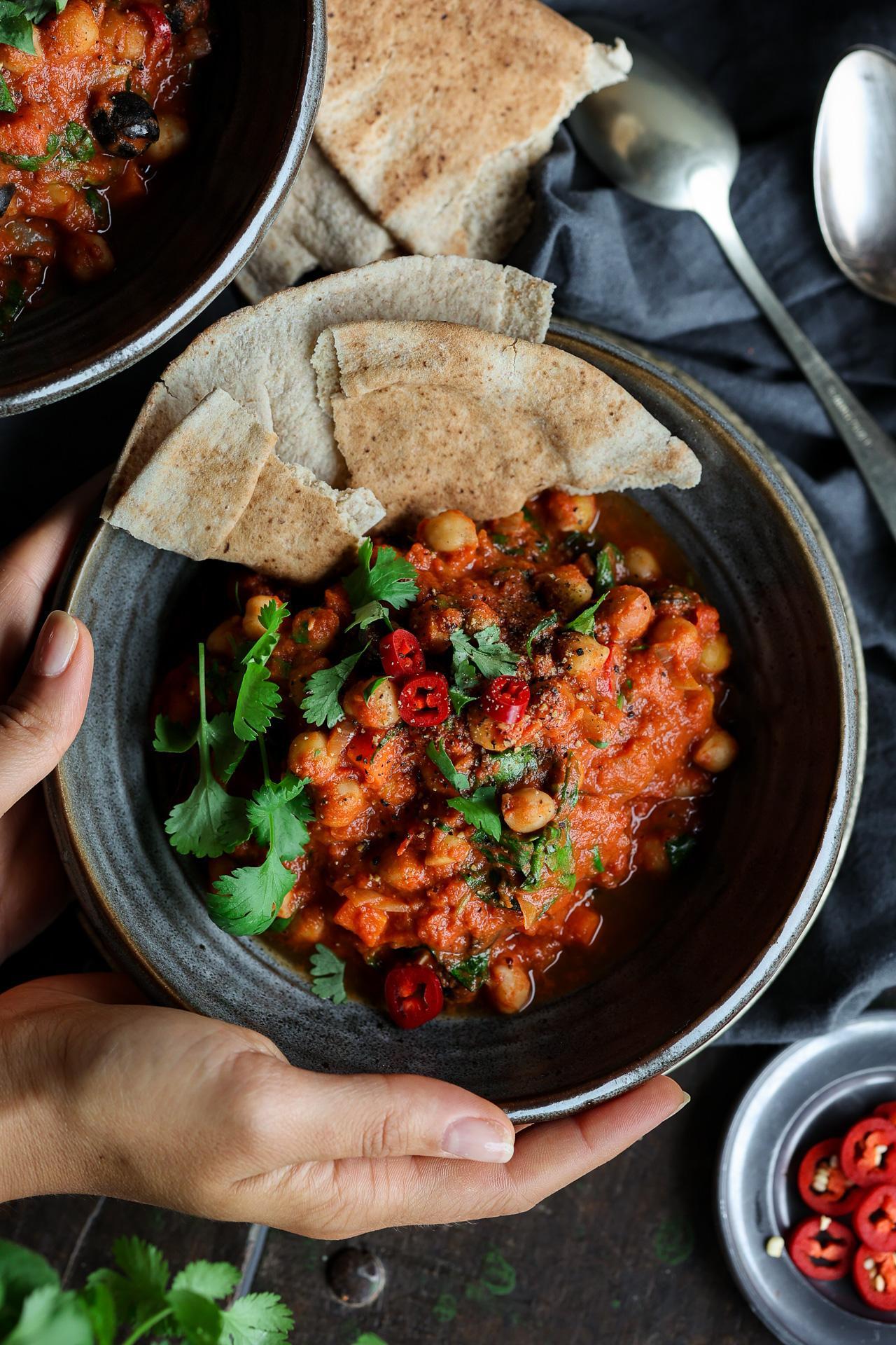 A person enjoying a bowl of tomato and chickpea curry outdoors