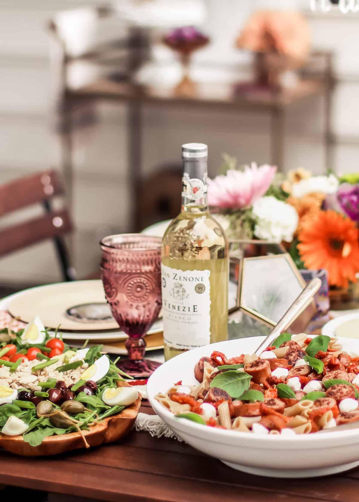 A rustic wooden table set with a bowl of Garlic Shrimp & Spinach Salsa Pasta, a glass of white wine, and crusty bread