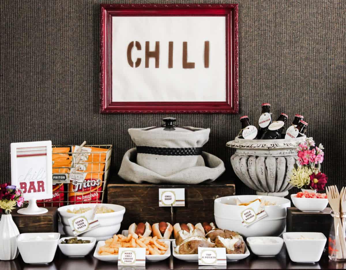 A table set with a bowl of chili cheese fries dip and various sides, including a basket of bread