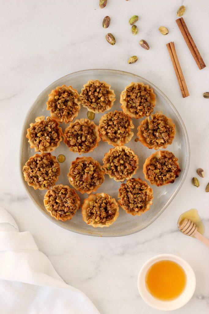A close up of a single mini baklava bite with a glistening honey syrup and a generous pistachio crumble topping