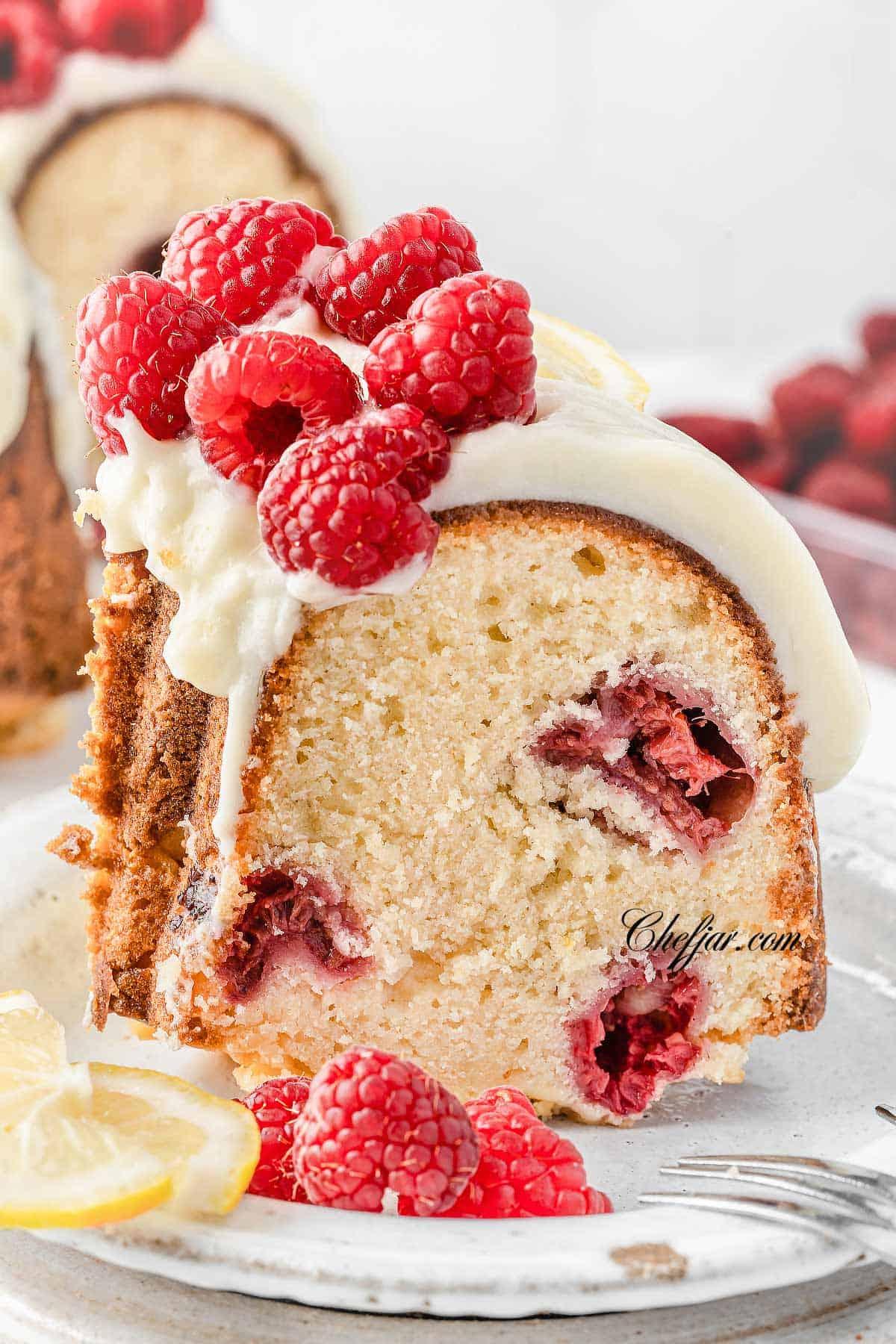 Lemon Raspberry Burst Cake on a cake stand, garnished with fresh raspberries and lemon slices
