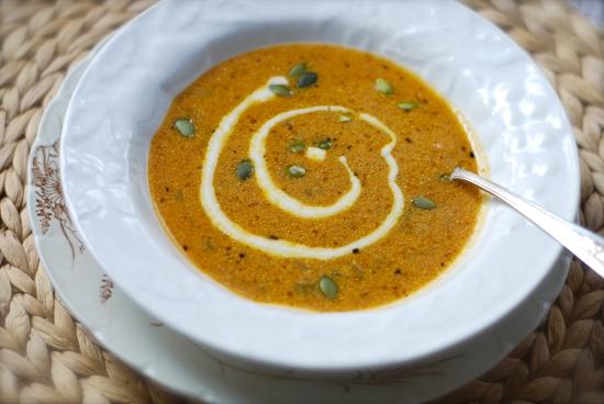 bowl of pumpkin soup garnished with chives and a drizzle of maple cream