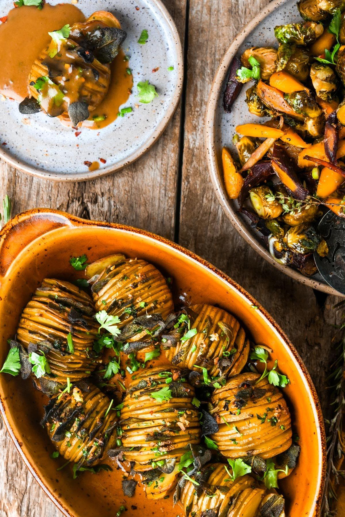 A rustic wooden table with a serving bowl of roasted potatoes, garnished with fresh herbs