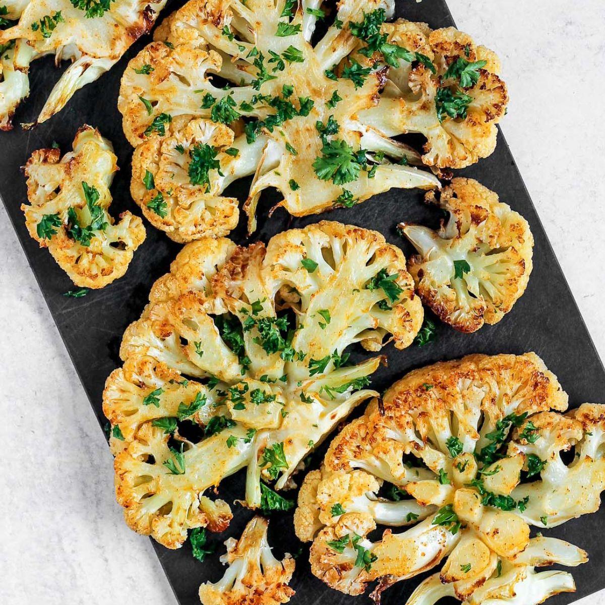 Close-up of seasoned cauliflower steaks and broccoli on a baking sheet