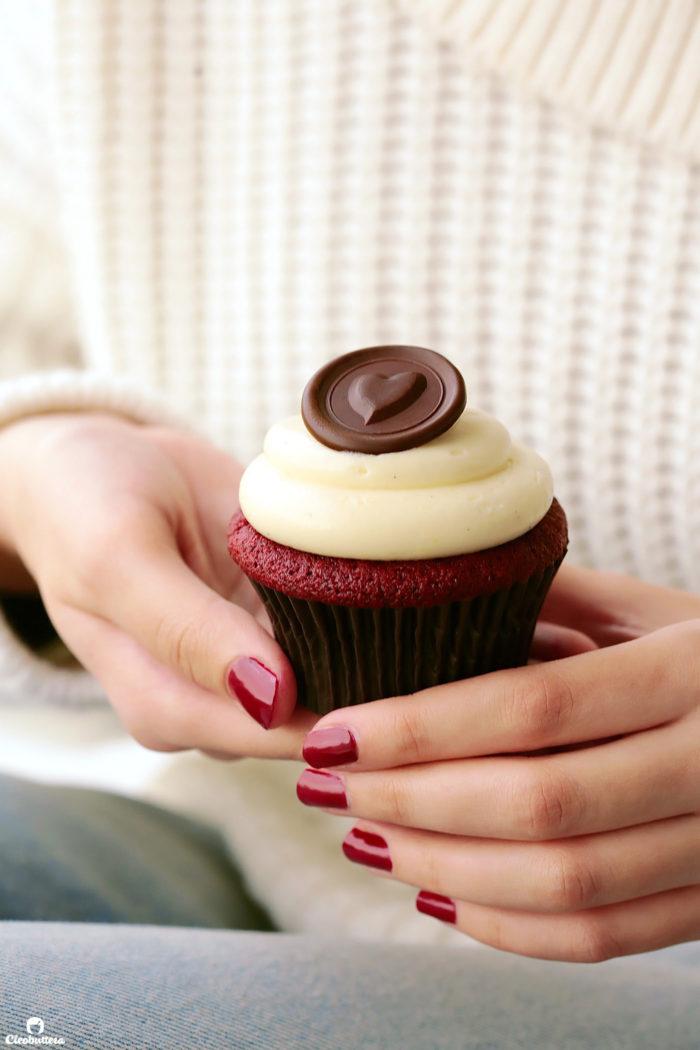 close up shot of someone sprinkling sprinkles on red velvet cupcake