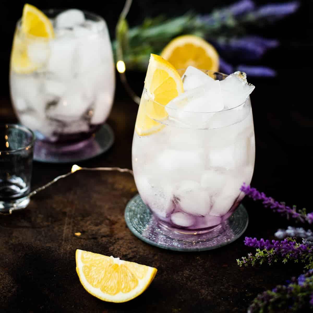 Close-up of a lavender kombucha spritzer in a glass with ice and lavender sprig garnish